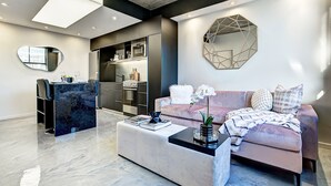 A modern living room with a marble floor, a sofa, a coffee table, and a kitchen area with built-in appliances. - Airy Apartment with All Amenities (Montreal)