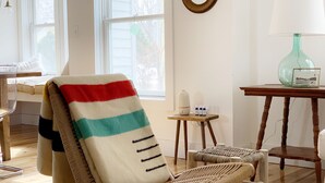 A room with a wooden chair covered with a striped blanket, a small table with a lamp, and a window with blinds. - Downtown! Huge 3,000 sq. ft Historic CVX Cottage, Sleeps 16! New Central A/C!!! (Charlevoix)
