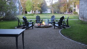 A gravel patio with a fire pit, surrounded by Adirondack chairs and a table. - Downtown! Huge 3,000 sq. ft Historic CVX Cottage, Sleeps 16! New Central A/C!!! (Charlevoix)