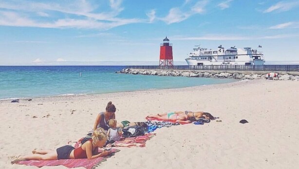 A beach with a red and white lighthouse and a white boat docked near the shore. - Downtown! Huge 3,000 sq. ft Historic CVX Cottage, Sleeps 16! New Central A/C!!! (Charlevoix)