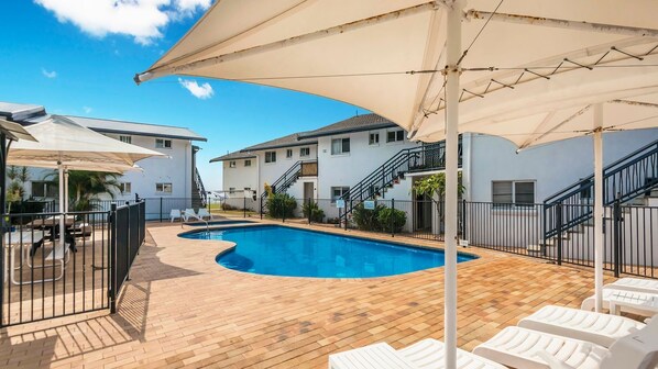 A swimming pool with a wooden deck, white lounge chairs, and a covered patio area. - 10T Beachfront Apartments (Lennox Head)
