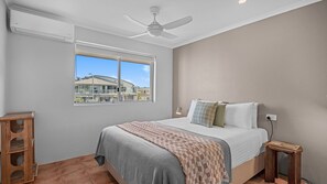 Une chambre à coucher avec un lit, une fenêtre, un ventilateur de plafond et une vue sur un bâtiment à l’extérieur.