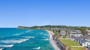 Un quartier résidentiel situé sur la côte, avec des maisons le long de la plage, un ciel dégagé et une vue sur l’océan.