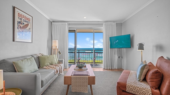 A hotel room with a balcony, a sofa, a TV, and a painting on the wall.