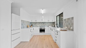 Een moderne keuken met witte kastjes, een centraal eiland en een achterwand van grijze tegels.