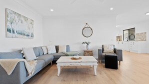 Een moderne woonkamer met een grijze bank, een witte salontafel en een keuken op de achtergrond.
