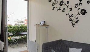 Ein Wohnzimmer mit einem grauen Sofa, einem Heizkörper und einer Wand mit schwarzen Blumenstickern.