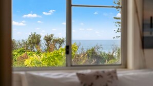 Une pièce dotée d’une grande fenêtre donnant sur un paysage côtier, avec une végétation luxuriante et la mer.