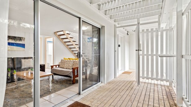 Un intérieur moderne avec une porte-fenêtre coulissante donnant sur un balcon, un escalier et un coin salon avec une table basse et des coussins.