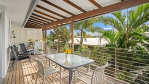 Une terrasse extérieure couverte, dotée d’une table et de chaises, entourée de plantes et offrant une vue sur des palmiers.