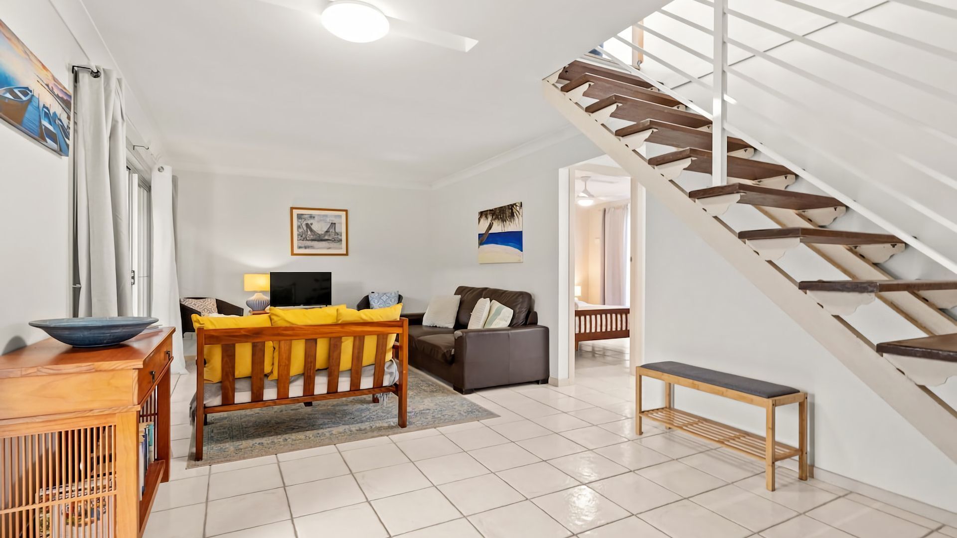 A spacious living room with a wooden staircase, a sofa, a coffee table, and a TV.
