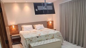 Een slaapkamer met een bed, een aan de muur bevestigde televisie en een raam met gordijnen.