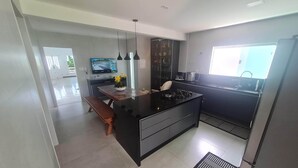 Een moderne keuken met een centraal eiland, zwarte kasten en een ingebouwde oven. Er is een raam dat natuurlijk licht biedt en een televisie aan de muur bevestigd.