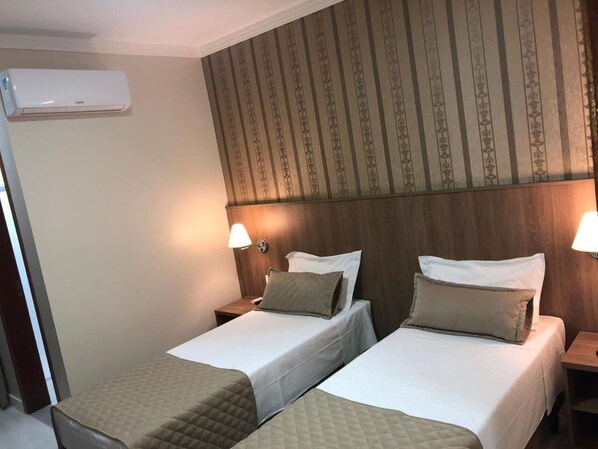A hotel room with two beds, a wooden headboard, and a wall-mounted air conditioner.