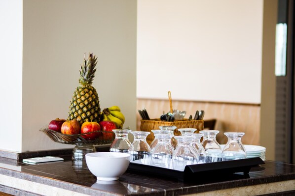 Une table de petit-déjeuner avec un saladier de fruits, un ananas et un panier d’ustensiles, le tout posé sur un comptoir en marbre.