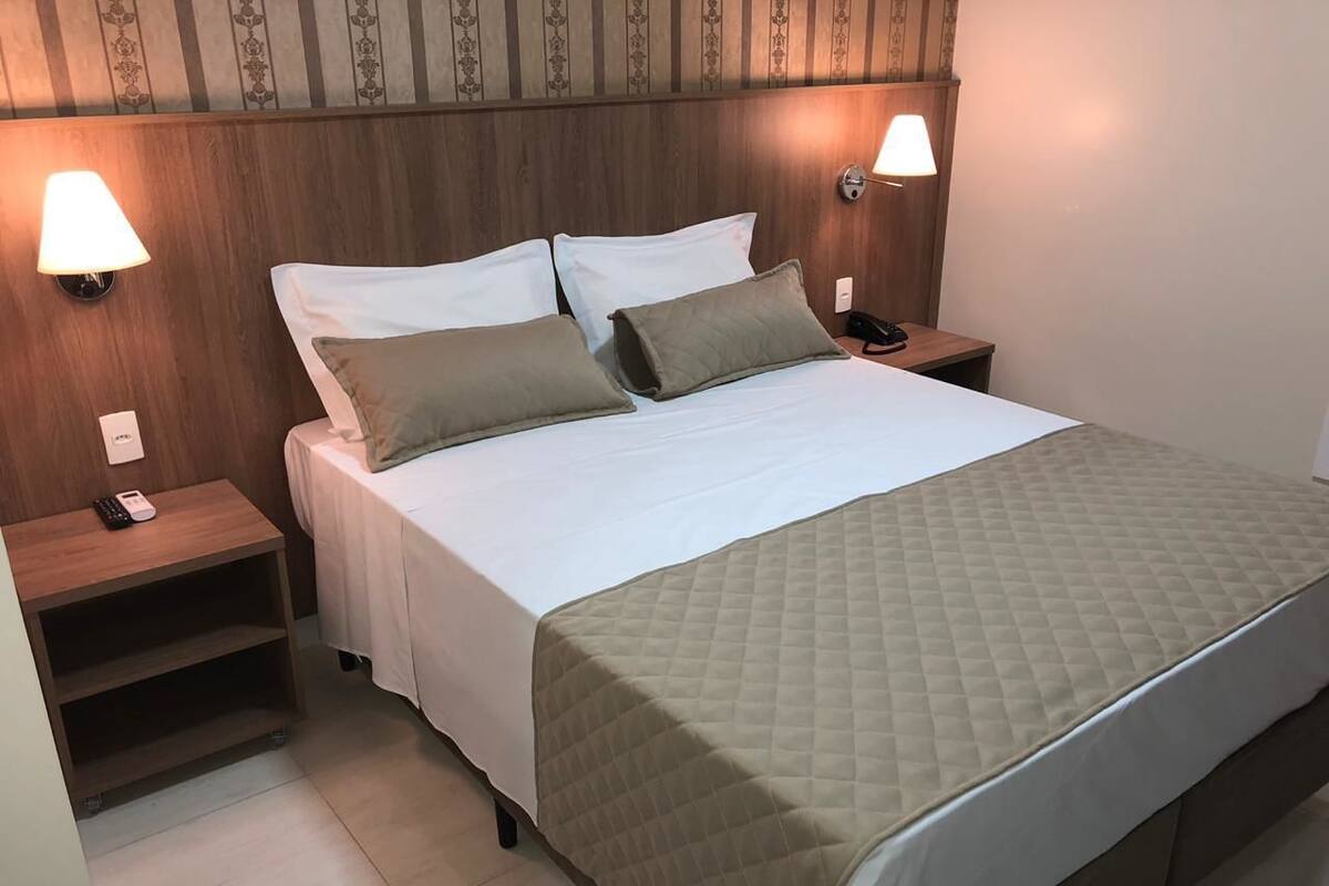 A neatly made bed with a quilted cover, two bedside tables with lamps, and a wooden headboard.