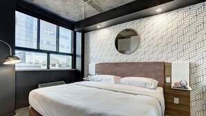 Une chambre d’hôtel moderne avec un grand lit, un miroir rond et un mur orné d’un motif géométrique.
