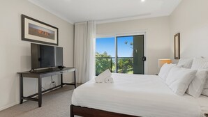 A hotel room with a bed, a TV on a stand, a painting on the wall, and a balcony with a view. - Surfside - Shelly Beach Holiday Home (East Ballina)