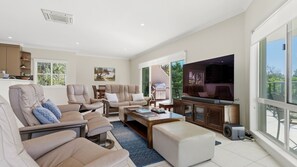 A spacious living room with a large flat-screen TV, comfortable seating, and a view of the outdoors.