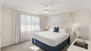 A hotel room with a large bed, two bedside tables with lamps, a ceiling fan, and sheer curtains.