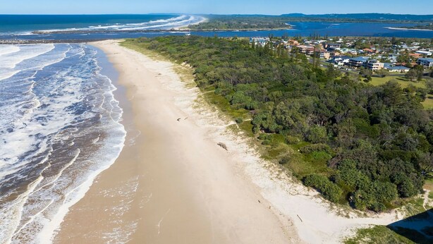 An aerial view of a beach with a forested area and residential buildings in the background.