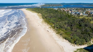 Vue aérienne d’une plage, avec une zone boisée et des immeubles résidentiels en arrière-plan.