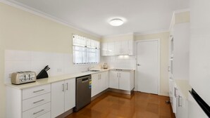 A compact kitchen with white cabinets, a toaster, a sink, and a dishwasher.