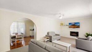 A modern living room with a grey sofa, a white coffee table, and a grey armchair. There is a fireplace, a TV mounted on the wall, and a painting above it.