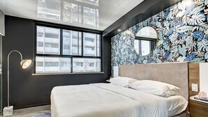 Un dormitorio moderno con una cama grande, una ventana que ofrece vistas a edificios y un papel tapiz con estampado floral.
