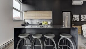 A modern kitchen with a marble countertop, wooden cabinets, and three bar stools. - THE YIN | One-Bedroom Loft w. Terrace (Montréal)