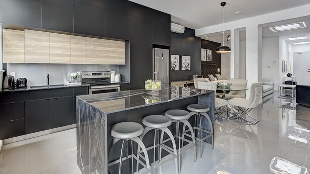 A modern kitchen with a central island, bar stools, and a dining area with a sofa and coffee table. - THE YIN | One-Bedroom Loft w. Terrace (Montréal)