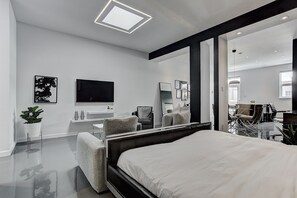 A modern hotel room with a large bed, a flat-screen TV, a seating area with chairs, and a large mirror. - THE YIN | One-Bedroom Loft w. Terrace (Montréal)