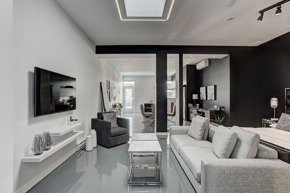 A modern living room with a flat-screen TV, a grey sofa, a coffee table, and a TV stand with decorative items. - THE YIN | One-Bedroom Loft w. Terrace (Montréal)