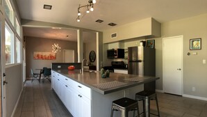A modern kitchen with a large island, stainless steel appliances, and a dining area with chairs. - Mid Century Desert Oasis - Walk to Tennis Garden, Coachella/Stagecoach shuttle! (Indian Wells)