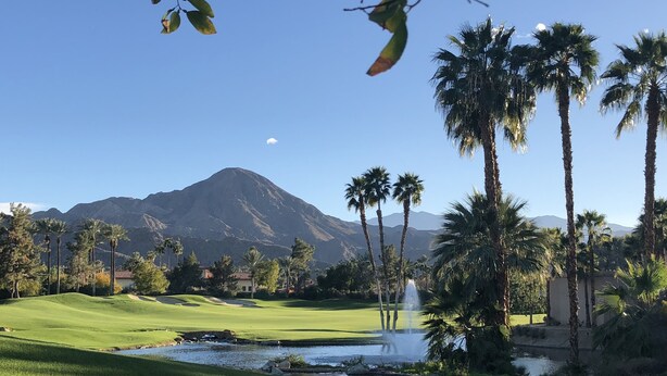 A golf course with a mountain in the background, palm trees, and a pond with a fountain. - Mid Century Desert Oasis - Walk to Tennis Garden, Coachella/Stagecoach shuttle! (Indian Wells)