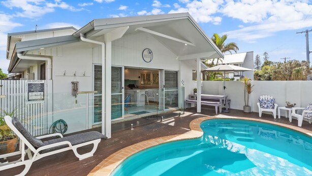 Una casa moderna con piscina, un patio cubierto y una cocina visible a través de puertas de cristal.