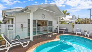 Ein modernes Haus mit Pool, einer überdachten Terrasse und einer durch Glastüren einsehbaren Küche.