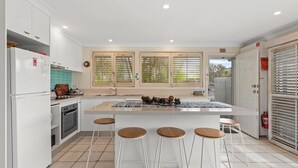 Una cocina moderna con armarios blancos, una isla central con taburetes, una estufa y un refrigerador.