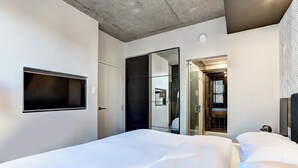 Een moderne hotelkamer met een groot bed, een flatscreen televisie aan de wand en een inloopkast met spiegel.