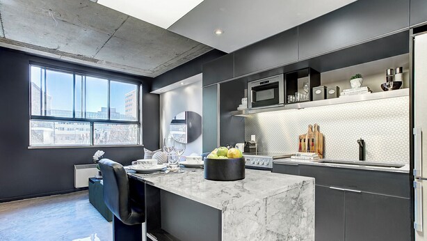 Een moderne keuken met een marmeren aanrechtblad, roestvrijstalen apparatuur en een stadszicht door grote ramen.