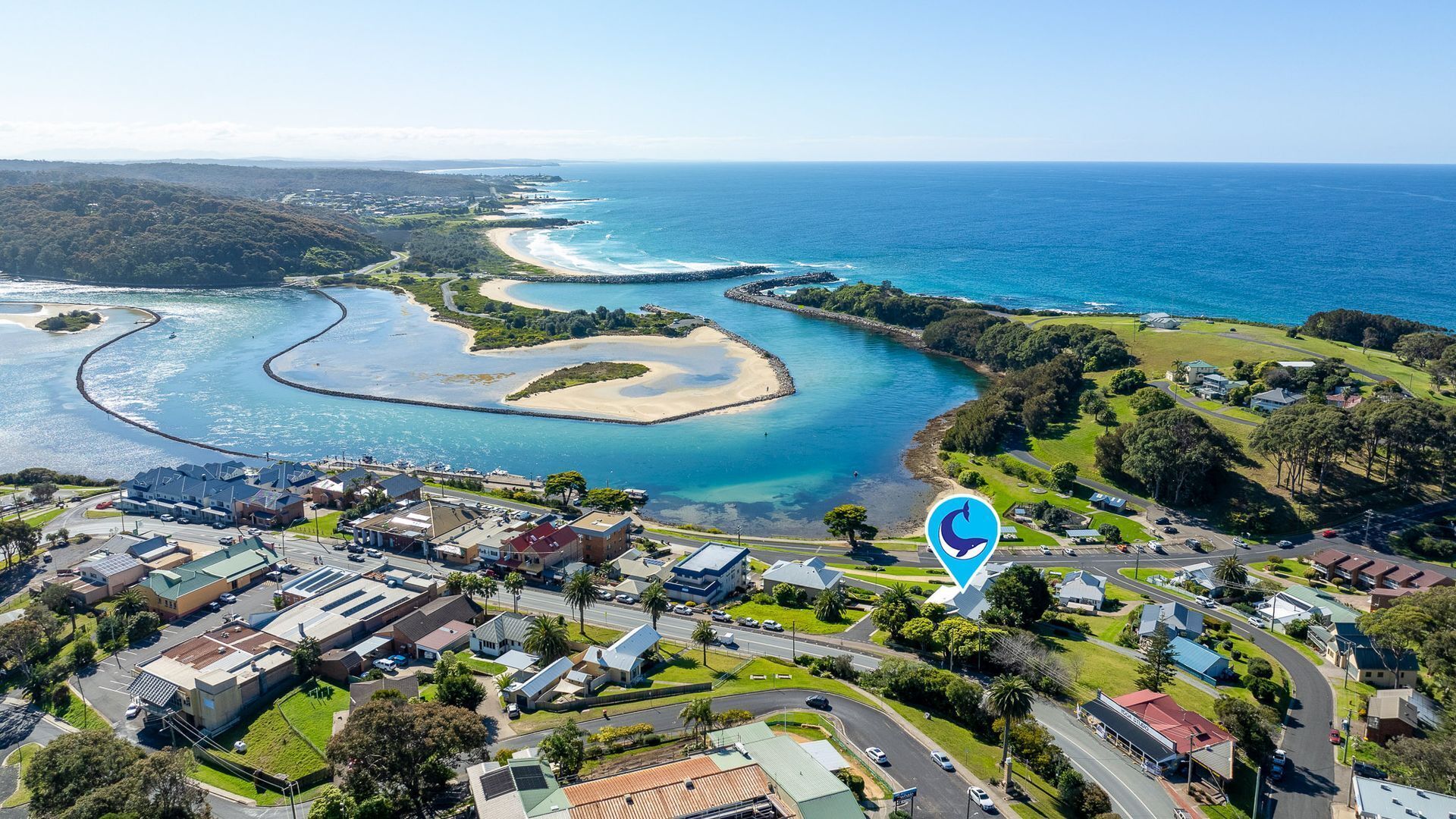 An aerial view of a coastal town with a marina, residential areas, and a prominent blue location marker.