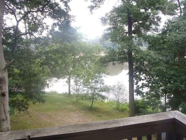 Une terrasse en bois donnant sur une zone boisée, avec un plan d’eau visible au loin.