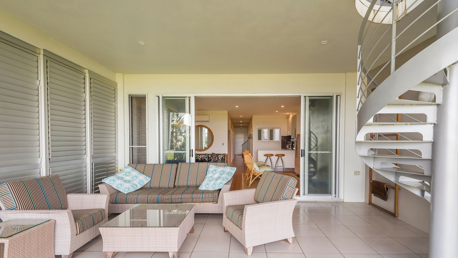 A spacious living area with a sofa set, a glass coffee table, and wicker chairs.