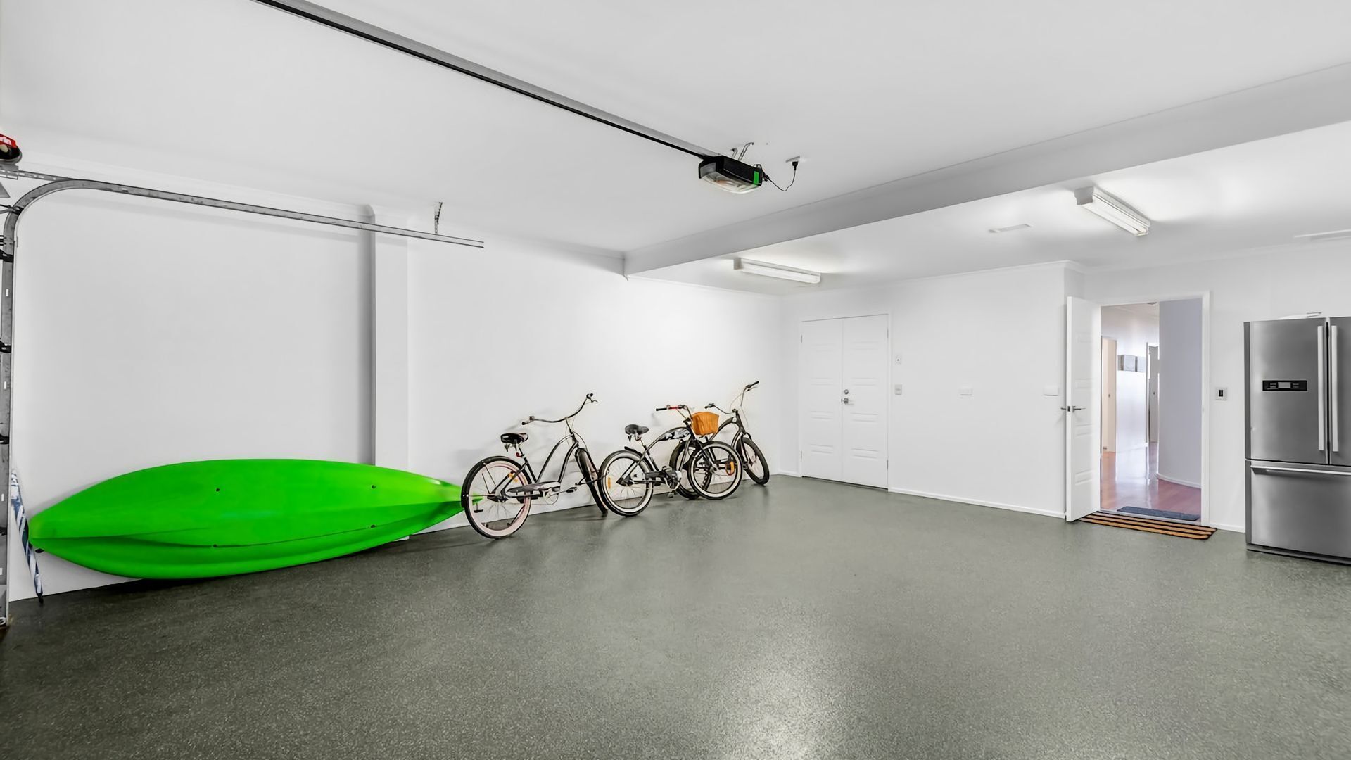 Amplia habitación moderna con un kayak verde, dos bicicletas y un refrigerador de acero inoxidable.
