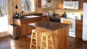 A kitchen with wooden cabinets, a granite countertop, a stainless steel trash can, a sink, a microwave, a stove, and two wooden stools. - Amazing lake views & access,HotTub & sauna, quality game Rm. 230-10 star Reviews (Wilmington)