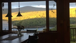 A dining area with a large window overlooking a forested landscape and a body of water. - Amazing lake views & access,HotTub & sauna, quality game Rm. 230-10 star Reviews (Wilmington)