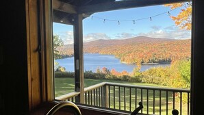 A view from a window with a wooden frame and a metal railing, overlooking a lake surrounded by autumn-colored trees and hills. - Amazing lake views & access,HotTub & sauna, quality game Rm. 230-10 star Reviews (Wilmington)