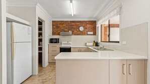 Una cocina con pared de ladrillo, armarios blancos, microondas, estufa y lavaplatos.