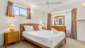 Una habitación de hotel con cama, mesitas de noche, ventilador de techo, espejo y cortinas.