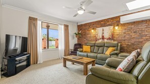 A living room with a television, a sofa, a coffee table, and a brick wall.